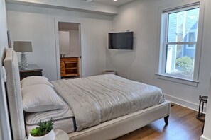 Un dormitorio con una cama, un televisor montado en la pared, una ventana y una planta pequeña.
