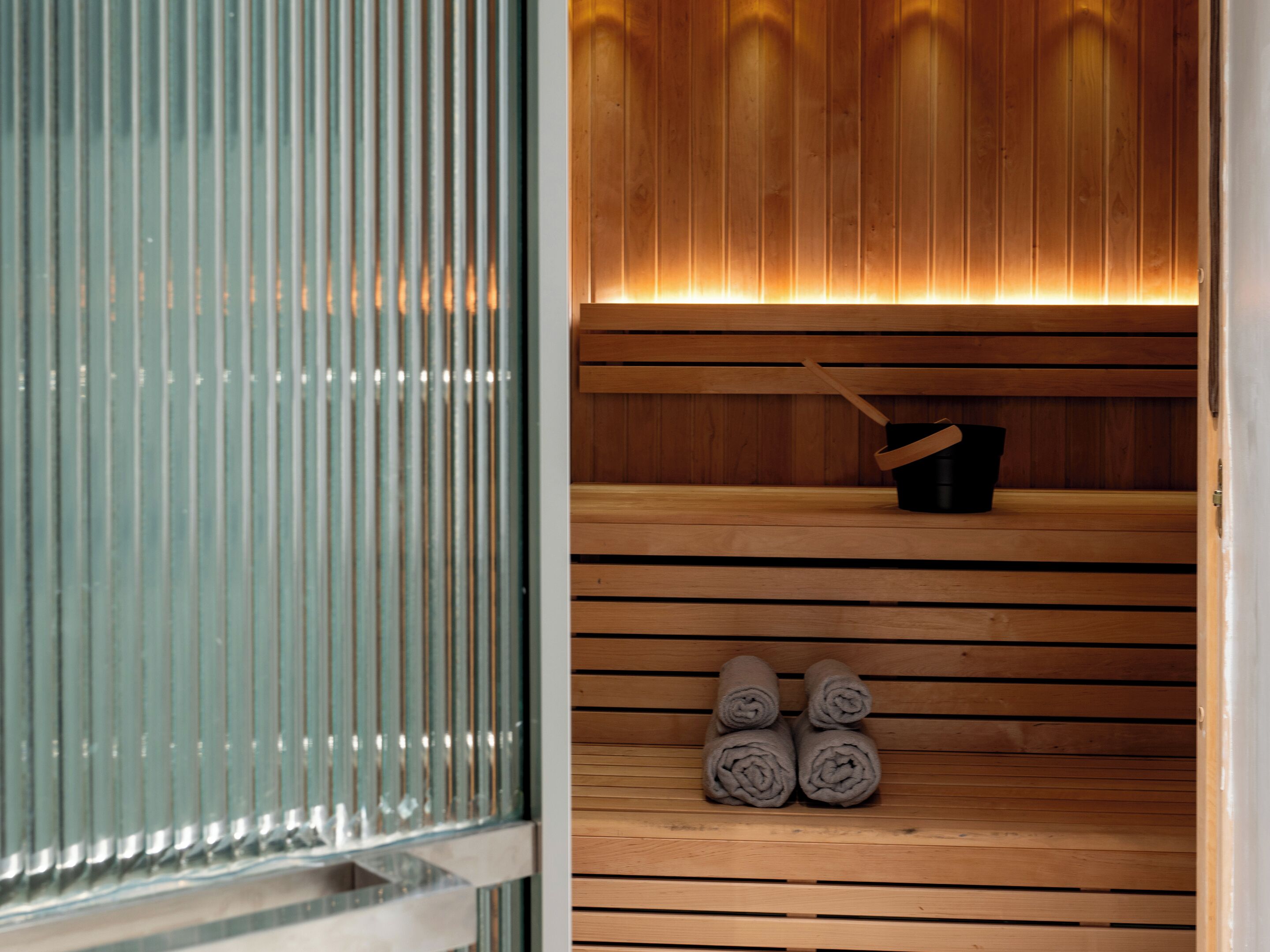 A sauna with wooden benches, a black bucket, and rolled towels.