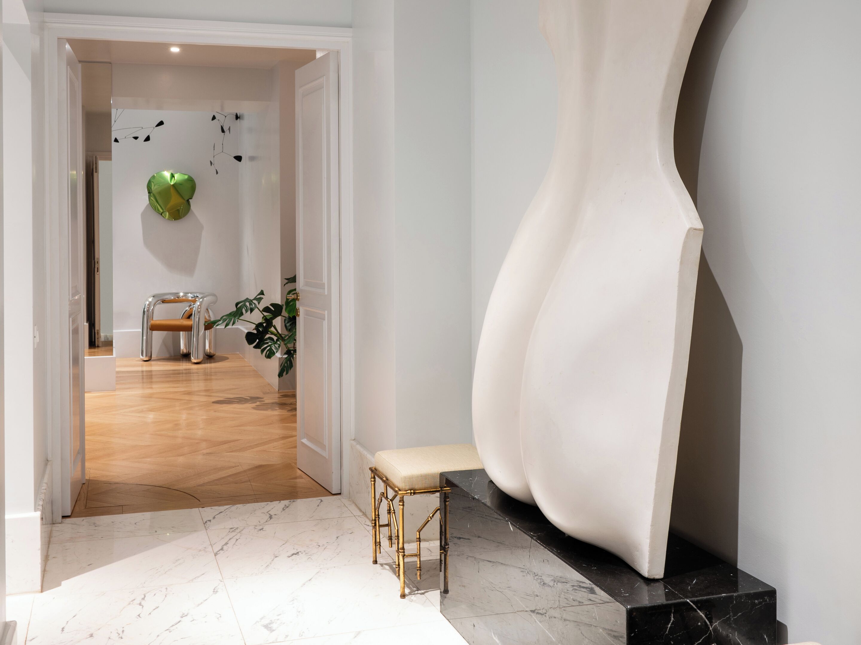 A modern interior with a marble floor, a bench, a large abstract sculpture, and a door leading to another room.