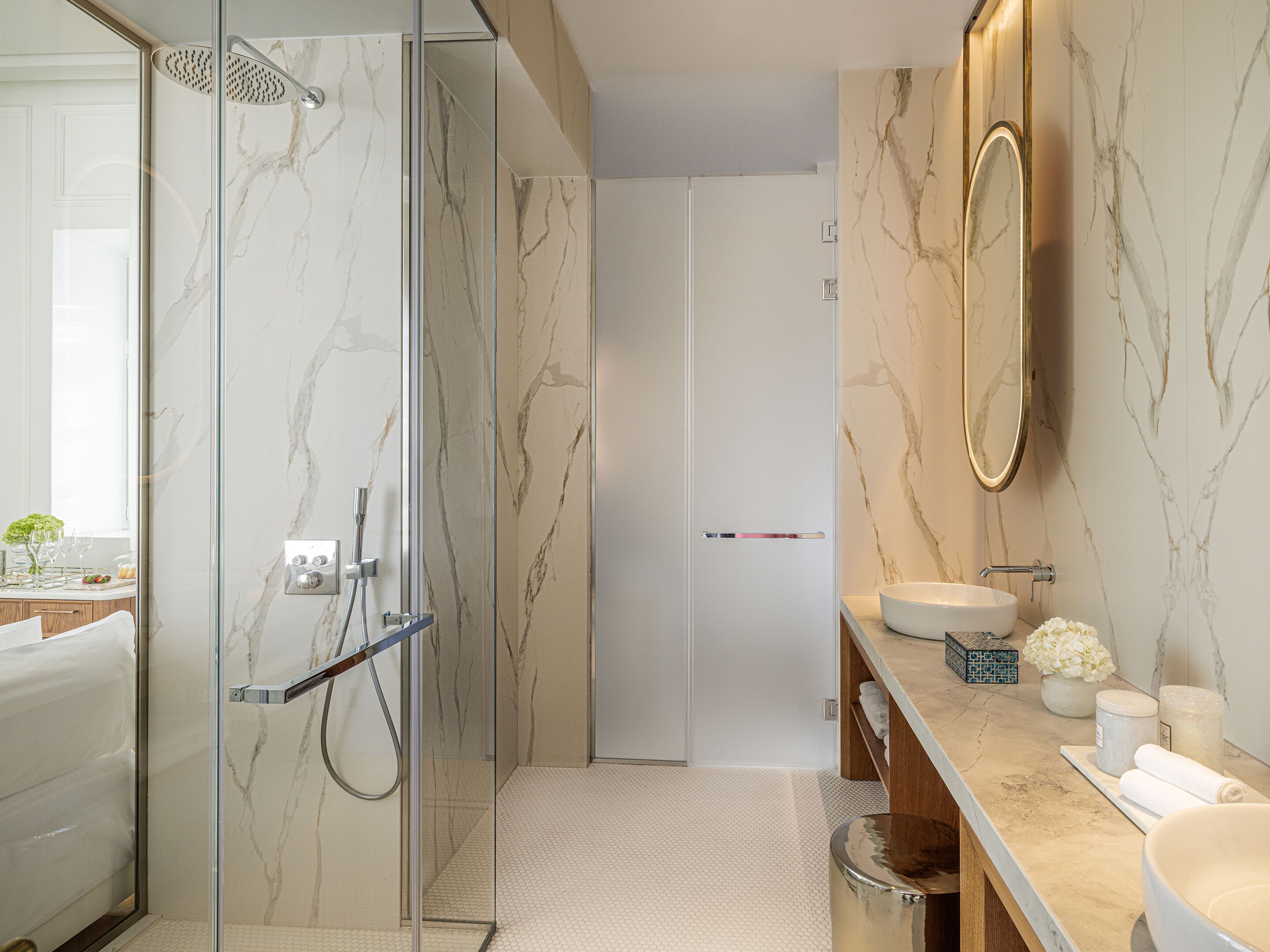 A modern bathroom with a glass-enclosed shower, a large mirror, and a marble-tiled wall.