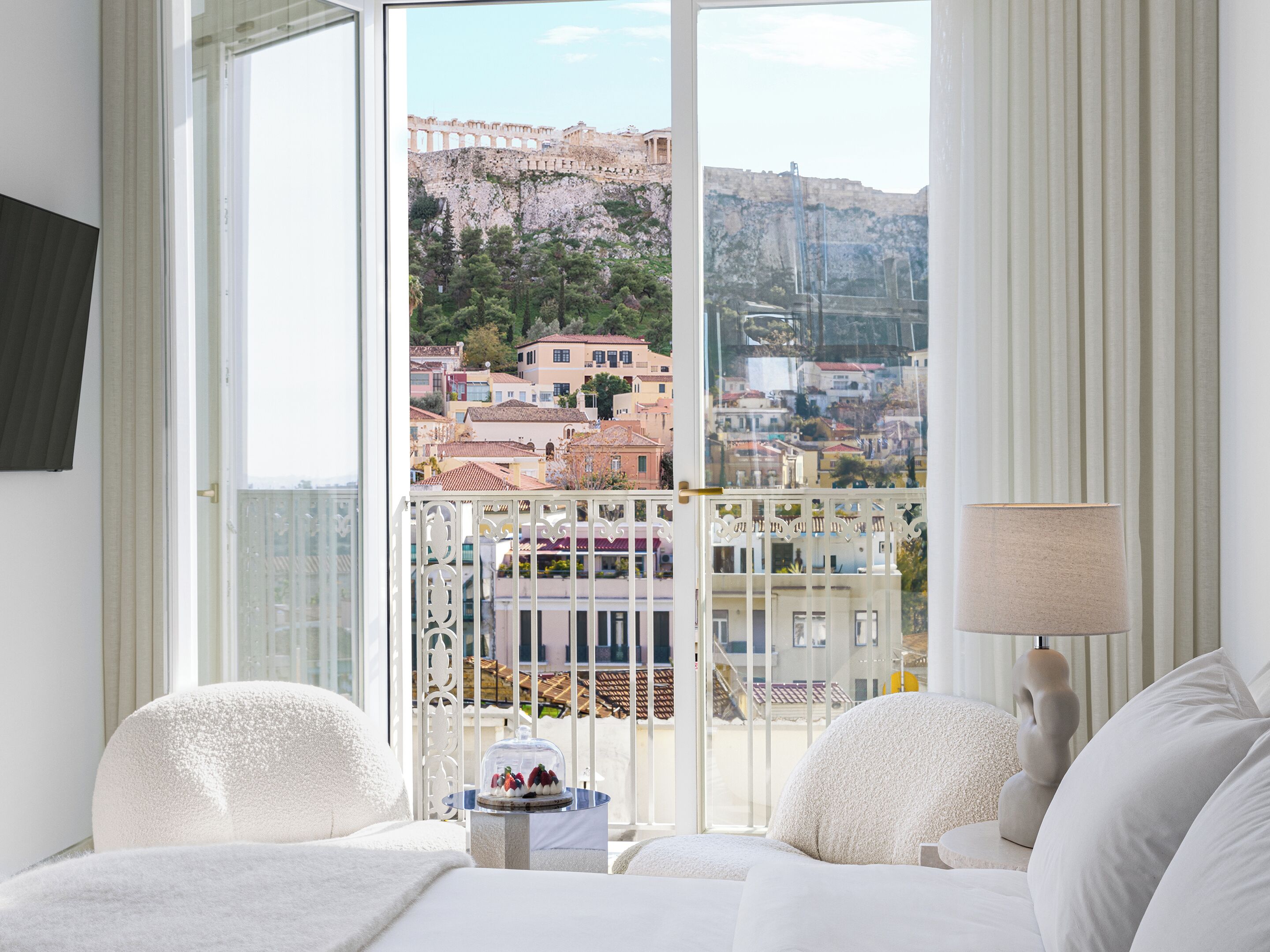 A hotel room with a balcony, a bed, a small table with a cake, and a lamp.