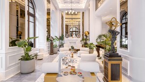 Un hall espacioso y elegantemente decorado, con techos altos, ventanas amplias y una zona de estar central con una mesa de centro.