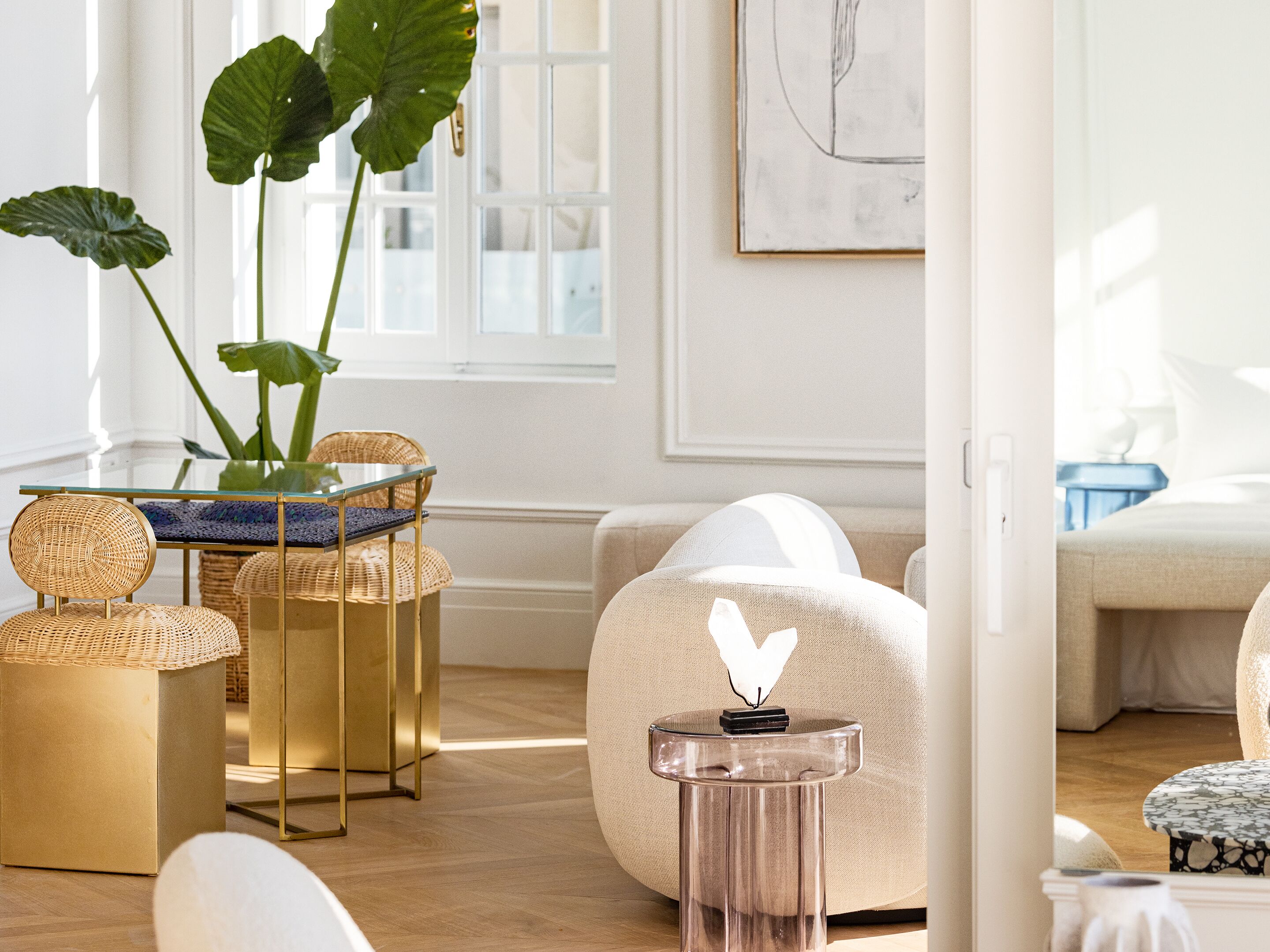 A well-lit room with a glass-top table, wicker chairs, a sofa, and a small side table with a decorative object.