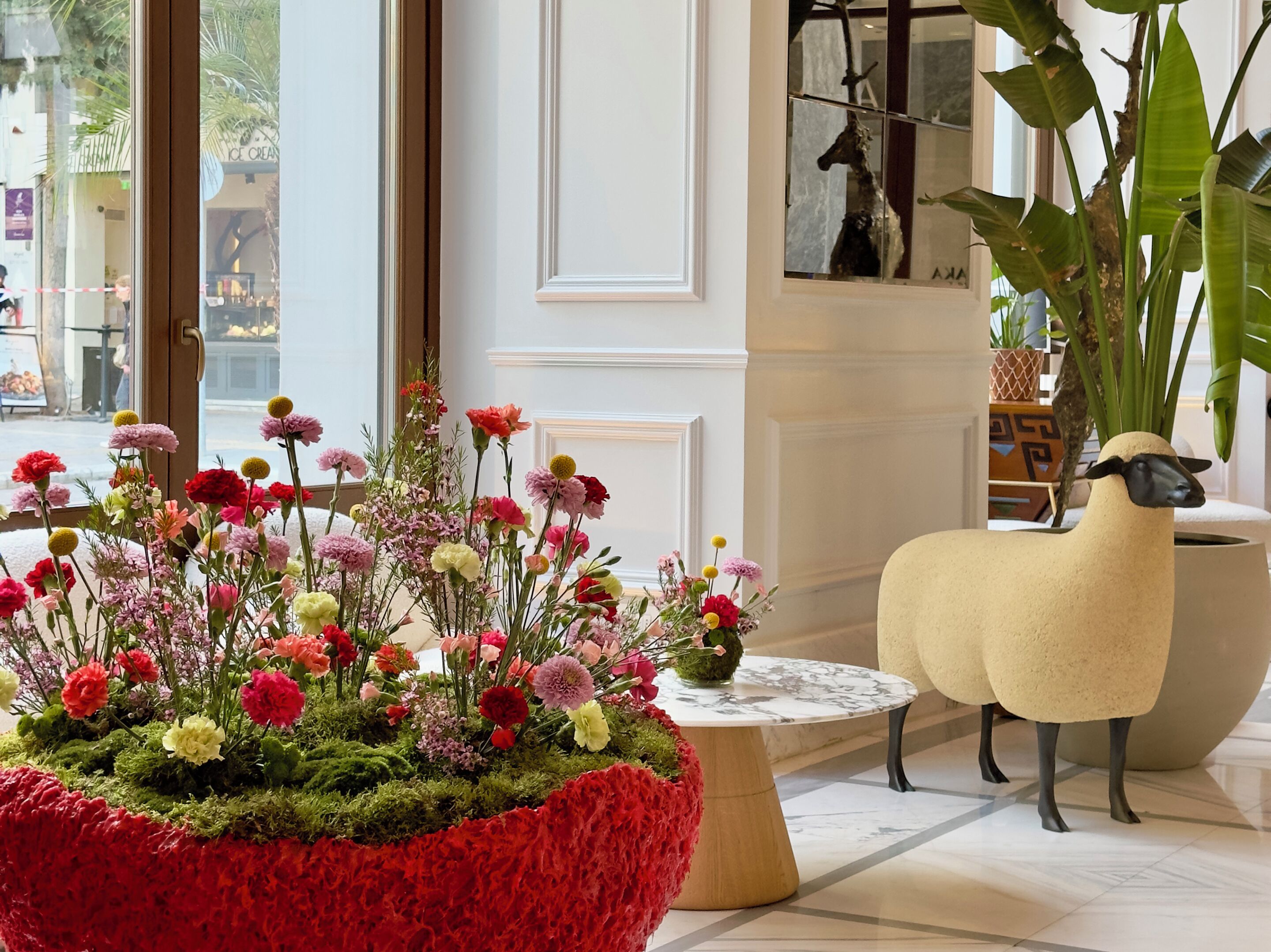 A room with a large floral arrangement, a round marble table, and a decorative sheep sculpture.