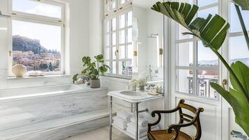 A bathroom with a marble floor, a sink, a chair, and a large window with a view of a town.