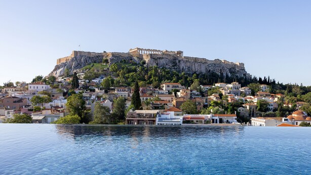 Un pueblo costero con una fortaleza histórica en una colina, aguas azules cristalinas y edificios residenciales.