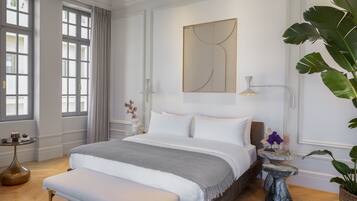 A modern bedroom with a large bed, bedside tables, a bench, and a large window with curtains.