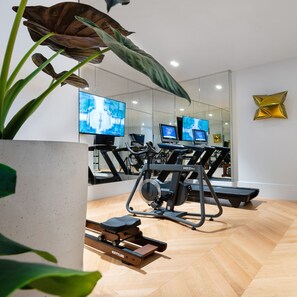 A modern gym with exercise equipment, large mirrors, and a large plant. - THE DOLLI at Acropolis, A Hotel to Live (Athens)