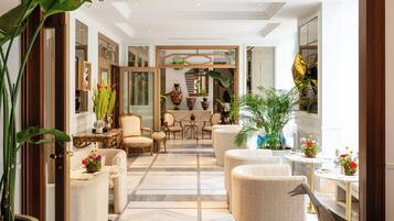 A spacious lobby with a high ceiling, marble flooring, and a variety of seating arrangements including armchairs and sofas.