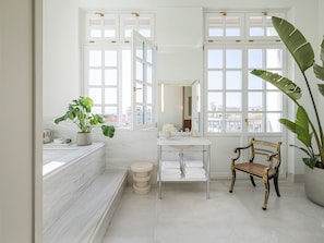 A bathroom with a marble sink, a bench, and large windows.