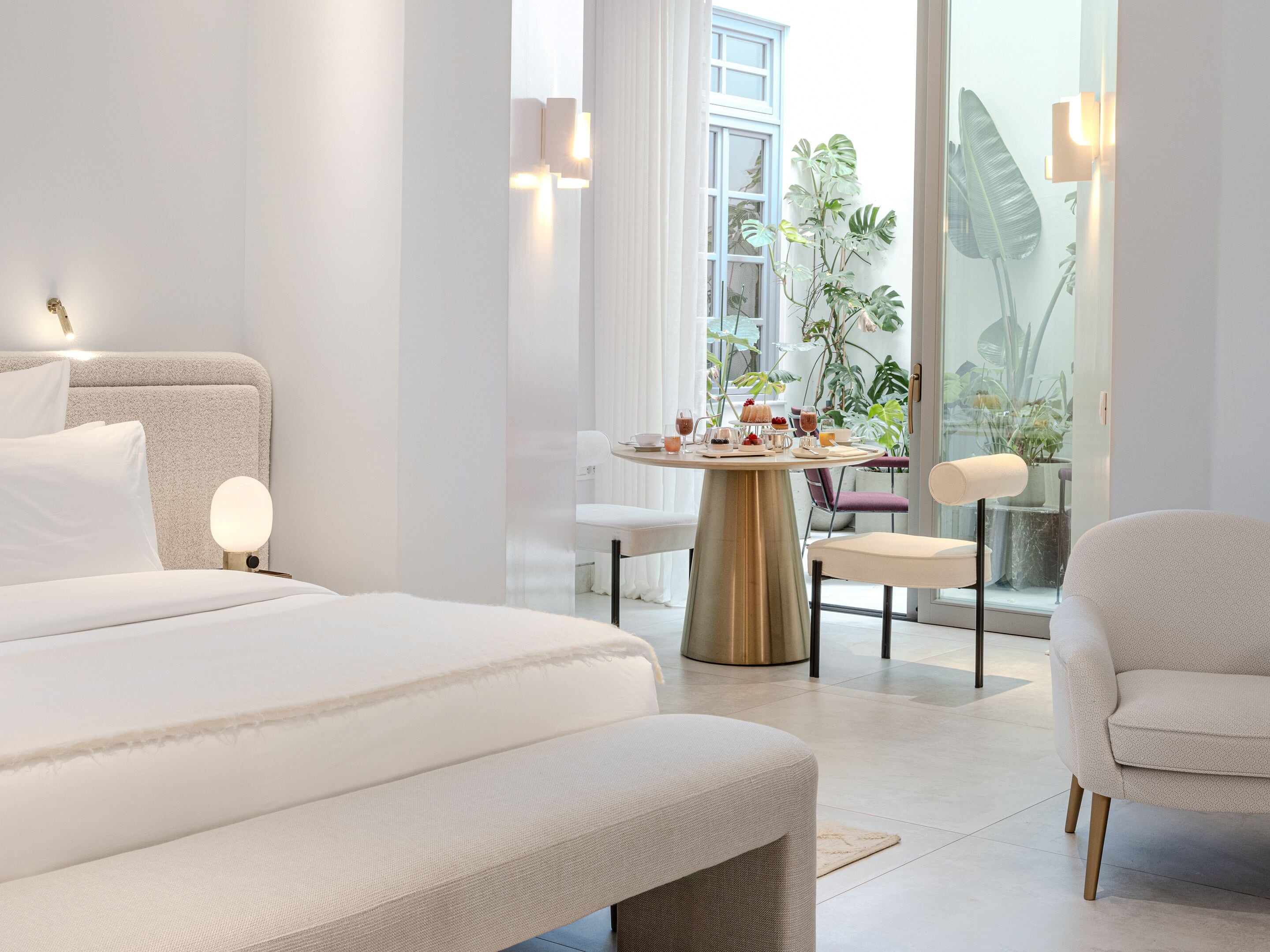 A modern hotel room with a large bed, a dining table with breakfast, and a view of the outdoors.