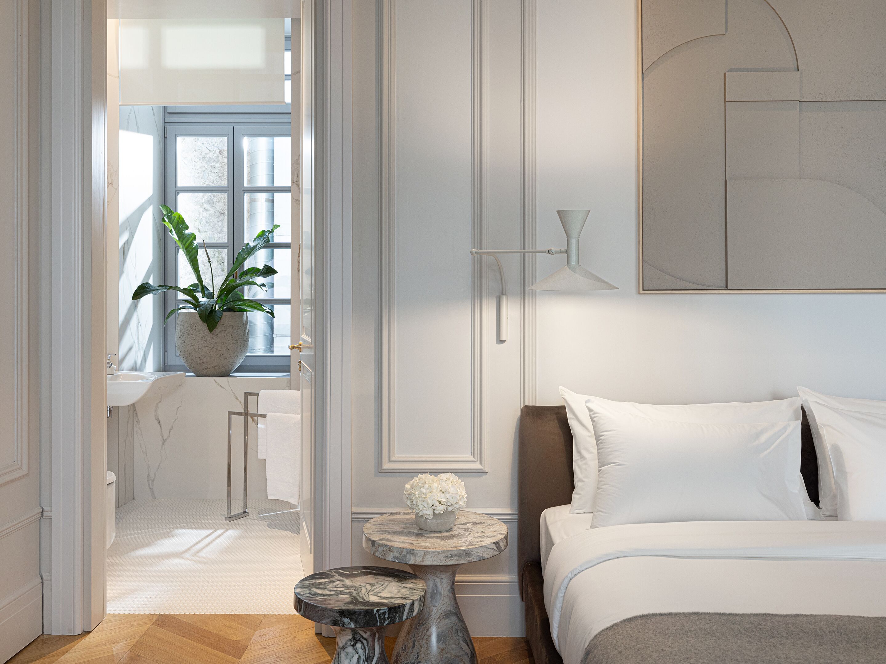 A modern bedroom with a bed, bedside table, and a potted plant by the window.