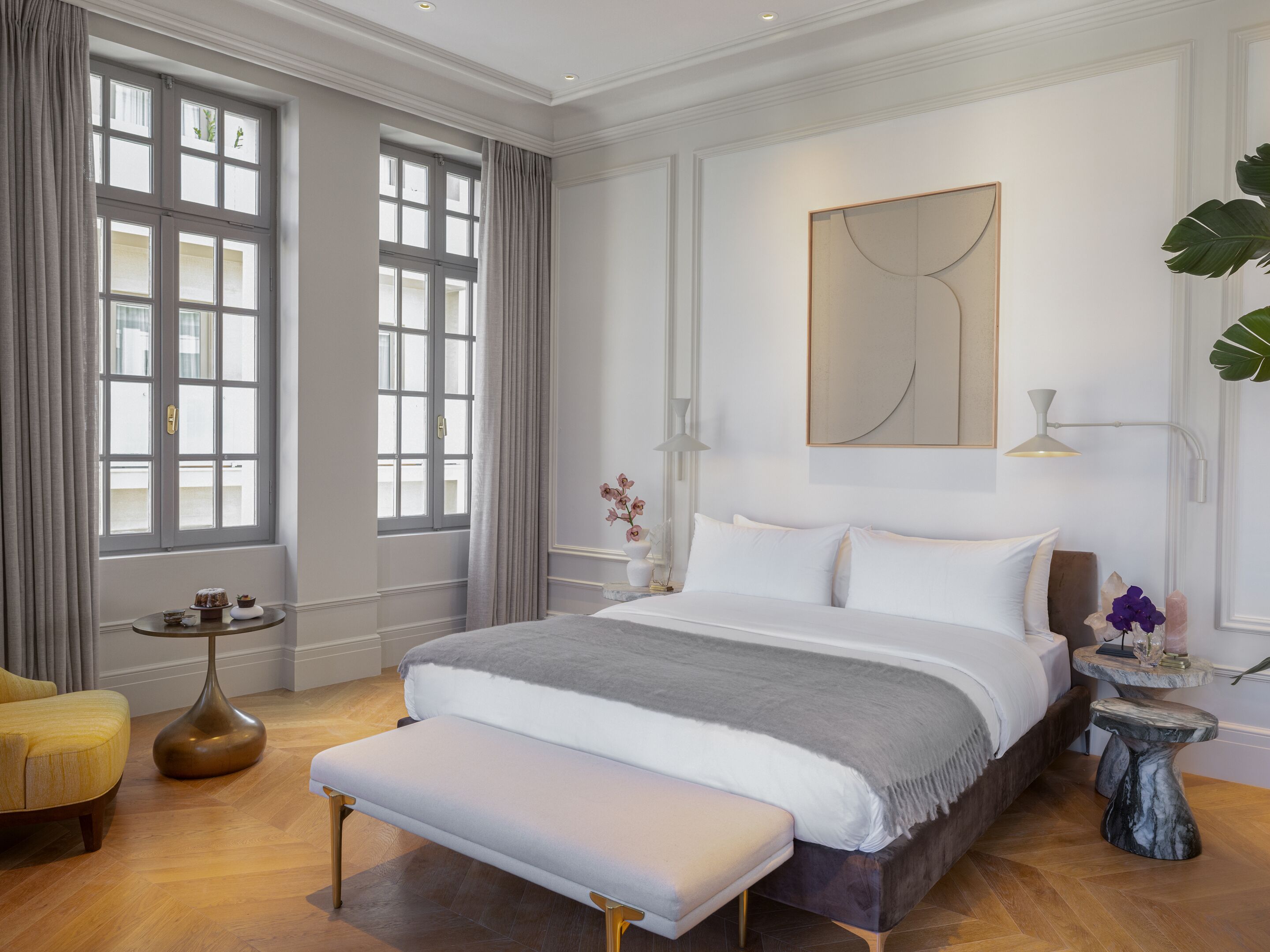 A spacious bedroom with a large bed, a bedside table, a bench, and a window with curtains.