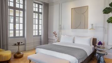 A spacious bedroom with a large bed, a bedside table, a bench, and a window with curtains.