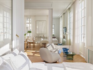 A spacious living room with a large window, a dining area, and a cozy seating area with a modern armchair and ottoman. - THE DOLLI at Acropolis, A Hotel to Live (Athens)