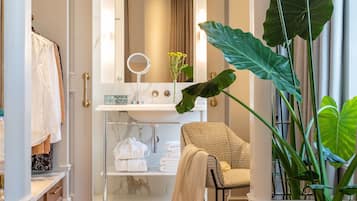A bathroom with a marble sink, a round mirror, a towel rack, and a chair.