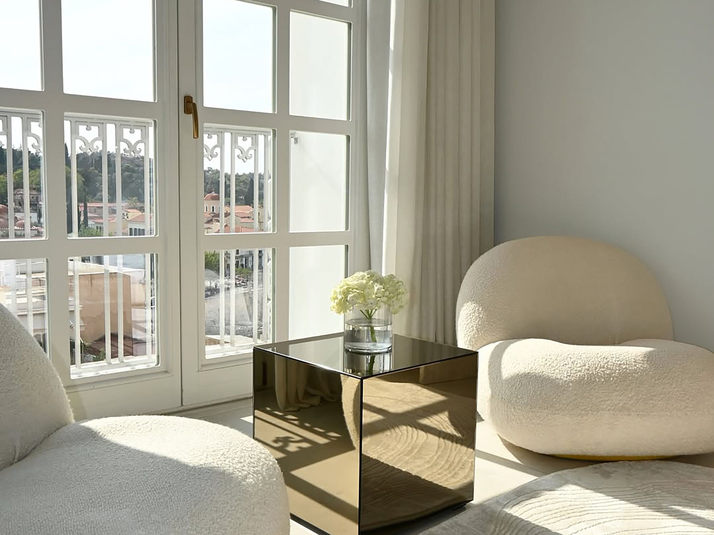 A room with a large window, a glass-topped table with a vase, a white chair, and a sofa.