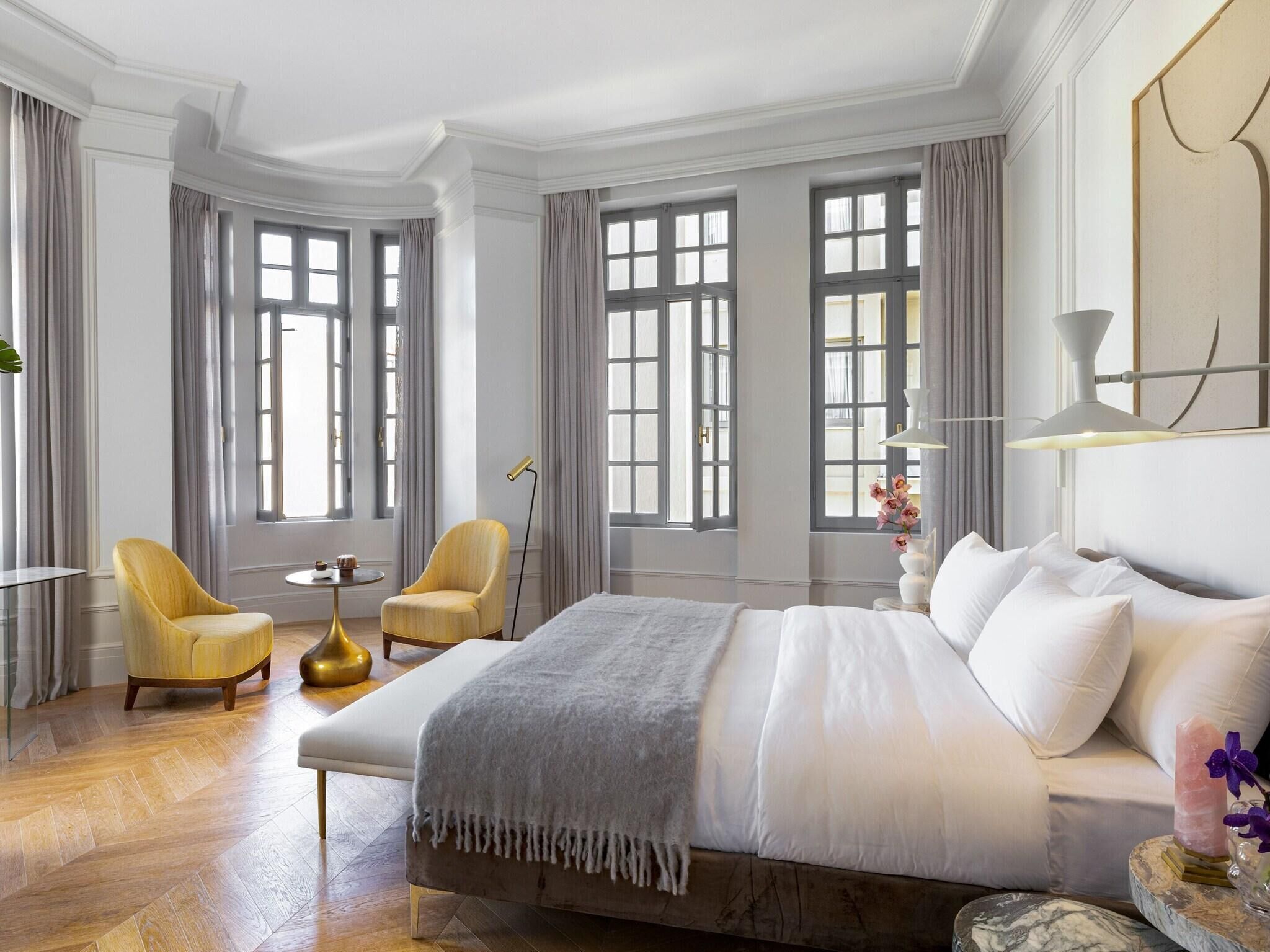 A spacious bedroom with a large bed, two armchairs, a small round table, and a floor lamp.