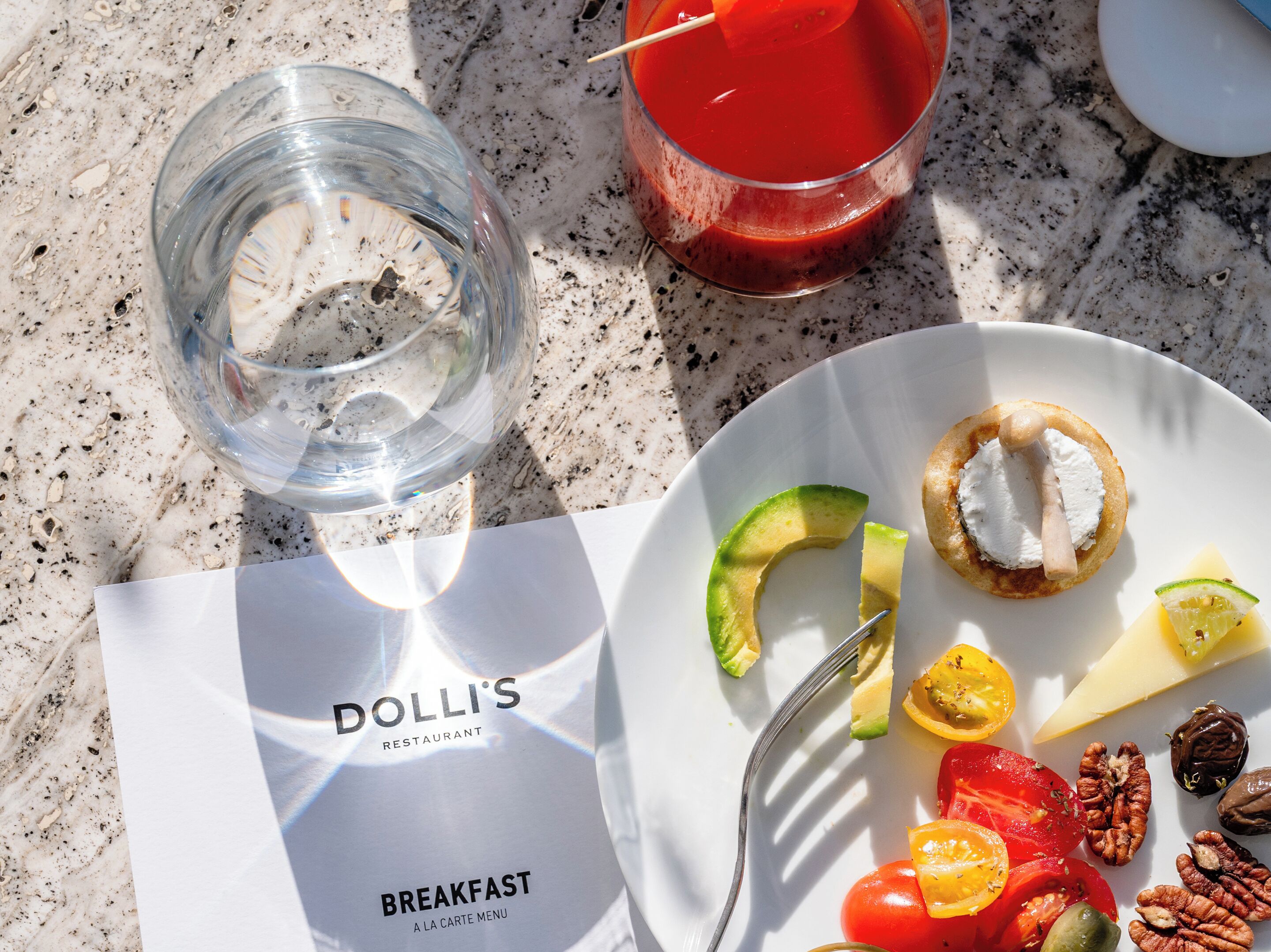 Menu della colazione del ristorante Dolli's, con un piatto di cibo che include avocado, formaggio, pomodori e noci.