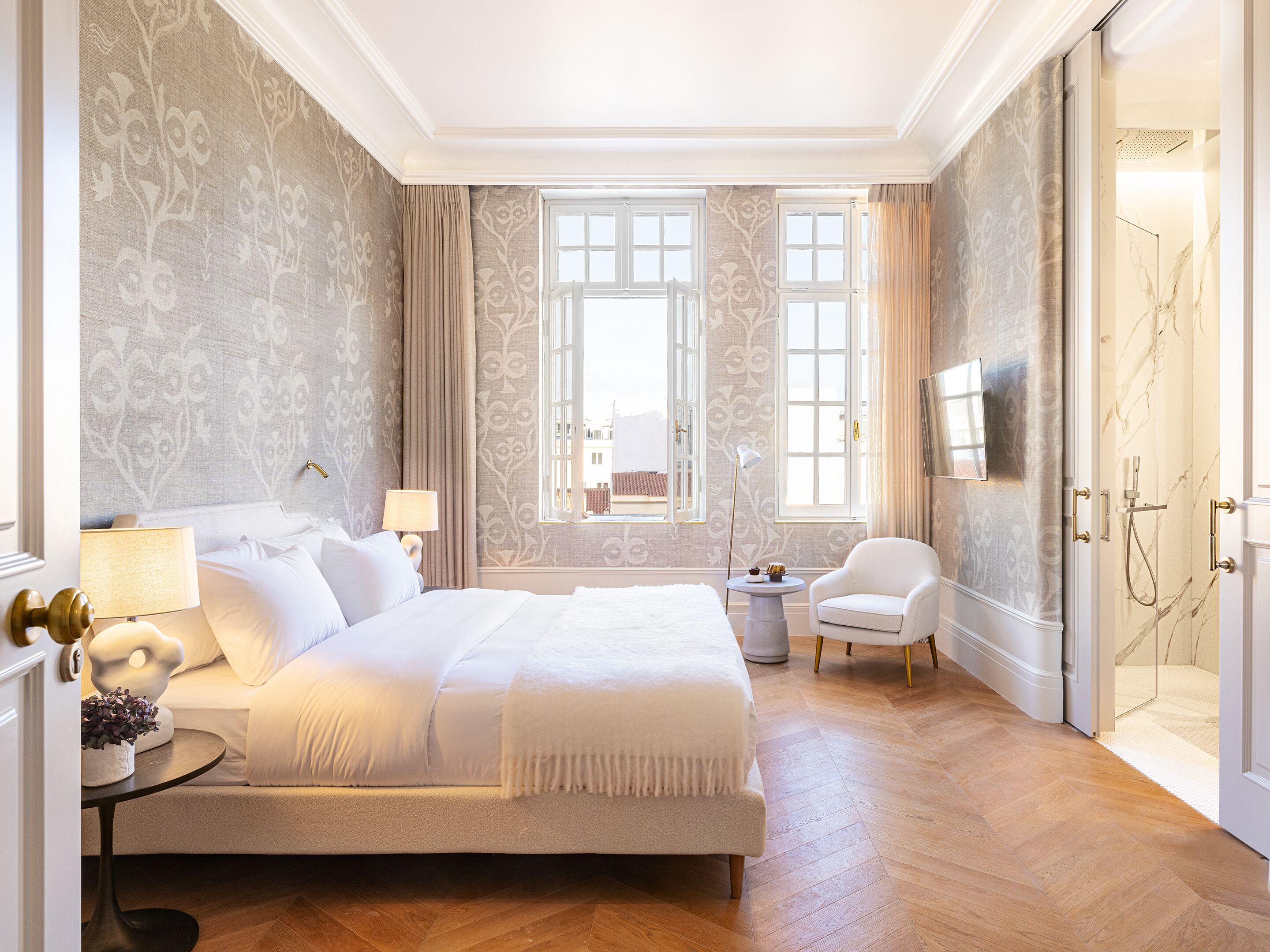 A spacious bedroom with a large bed, a sitting area with a chair, and a shower area.