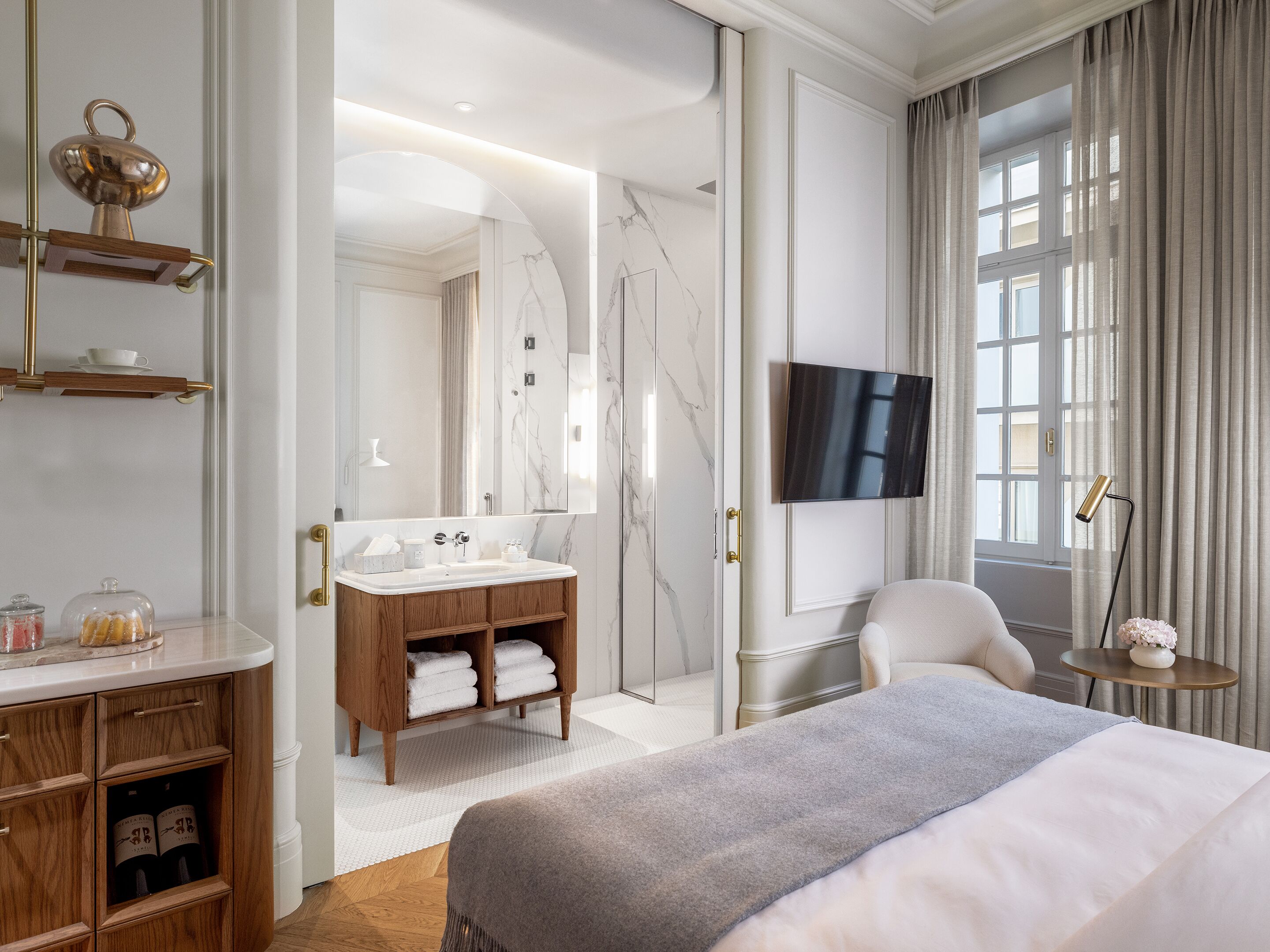 A hotel room with a bed, a TV, a bathroom with a mirror, and a window with curtains.