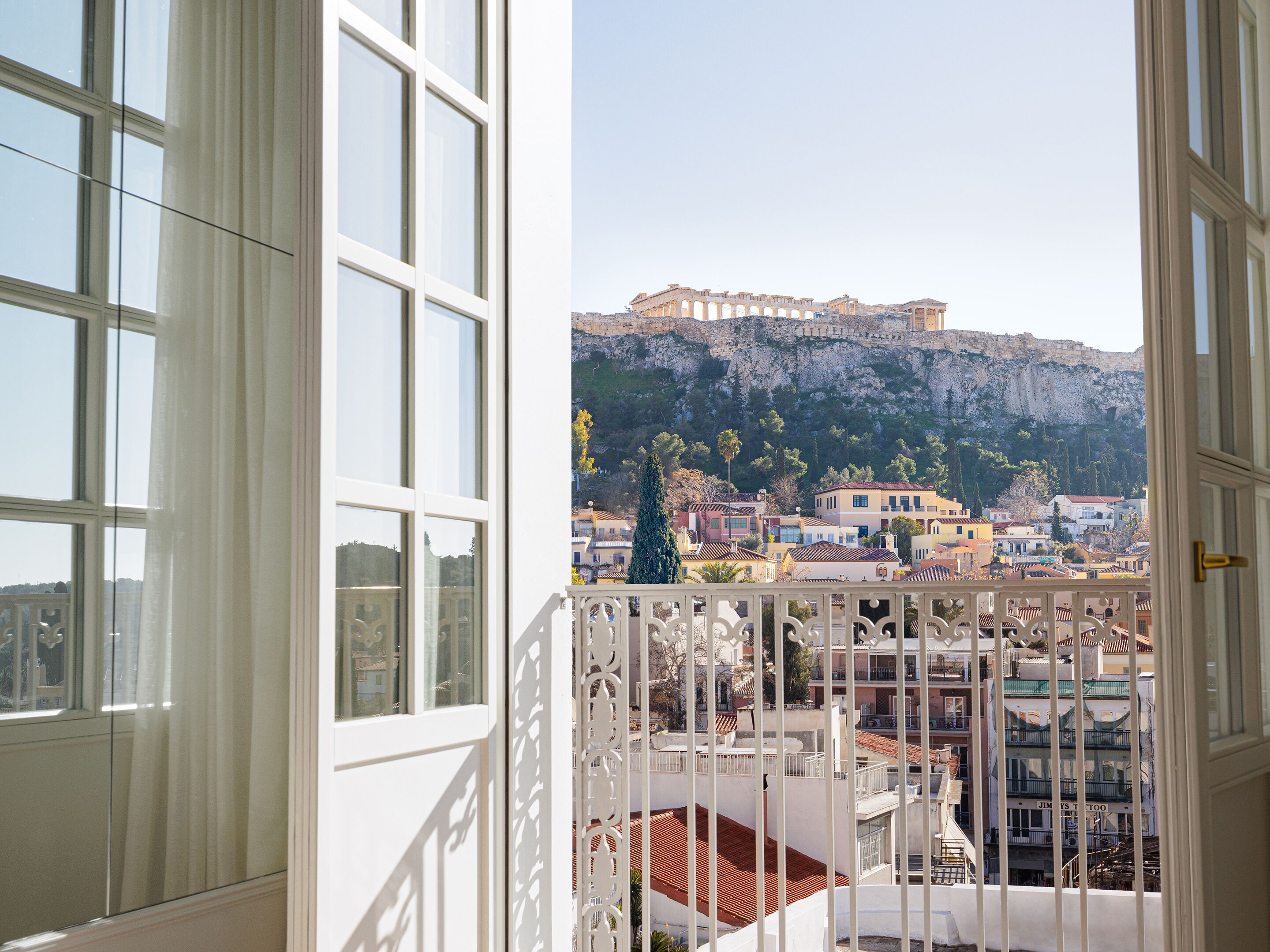 Une vue depuis un balcon doté d’une balustrade blanche, donnant sur une ville avec ses bâtiments et une imposante structure antique située sur une colline.