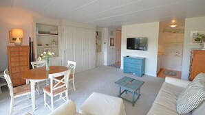 Un salon comprenant une table à manger, des chaises, un canapé, un téléviseur et une commode bleue.