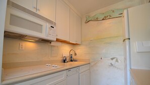 Une cuisine avec des meubles blancs, un four à micro-ondes, un évier et un réfrigérateur.