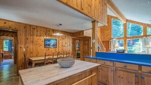 A wooden cabin interior with a dining area, a kitchen with a blue countertop, and large windows. - Stargazer Chalet in Carnelian Bay (Carnelian Bay)