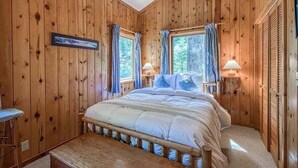 A wooden-paneled bedroom with a bed, two bedside lamps, and a framed picture on the wall. - Stargazer Chalet in Carnelian Bay (Carnelian Bay)