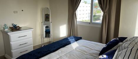 Quarto com cama, penteadeira, espelho e janela com cortinas.