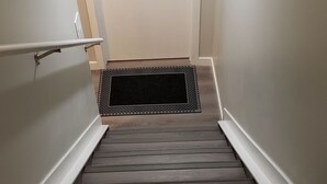 En trætrap med en sort dørmåtte forneden, der fører op til en hvid dør.