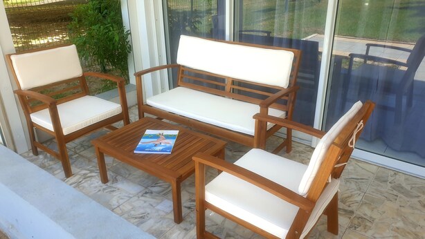 A wooden outdoor seating area with white cushioned chairs and a matching bench, featuring a book on the table. - Le grand saint martin II (Marigot)