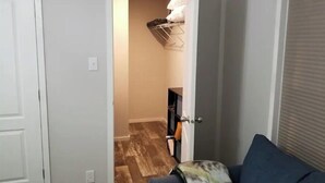 Ein Zimmer mit einem blauen Sofa, Holzboden und einem Kleiderschrank mit Kleidung.