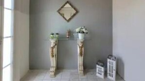 Una stanza con una parete grigia, un tavolino con un vaso di fiori e uno specchio decorativo.