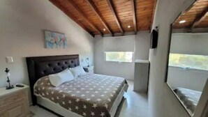 Una camera da letto con soffitto in legno, un letto con copriletto a motivi stellati, un comodino, una TV a parete e una finestra.