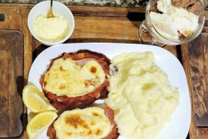 Une assiette contenant deux steaks, recouverts de fromage, accompagnés de purée de pommes de terre et de quartiers de citron.
