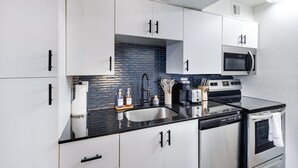A modern kitchen with white cabinets, a black countertop, a stainless steel stove, and a microwave above the stove. - Bar, restaurants, and attractions all nearby! (Phoenix)