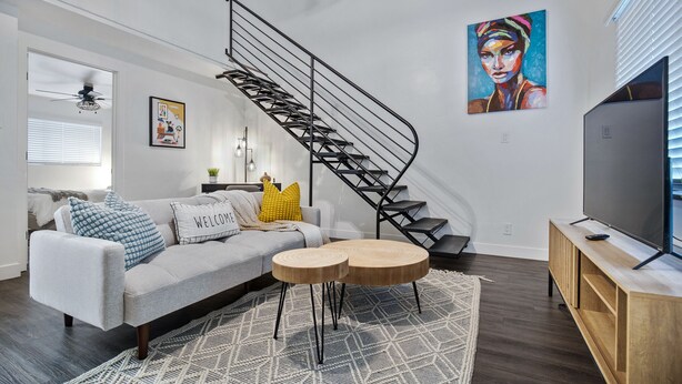 A modern living room with a grey sofa, a wooden coffee table, a TV on a wooden stand, a spiral staircase, and a painting on the wall. - Bar, restaurants, and attractions all nearby! (Phoenix)