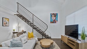 A modern living room with a staircase, a sofa, a coffee table, a TV, and a painting on the wall. - Bar, restaurants, and attractions all nearby! (Phoenix)
