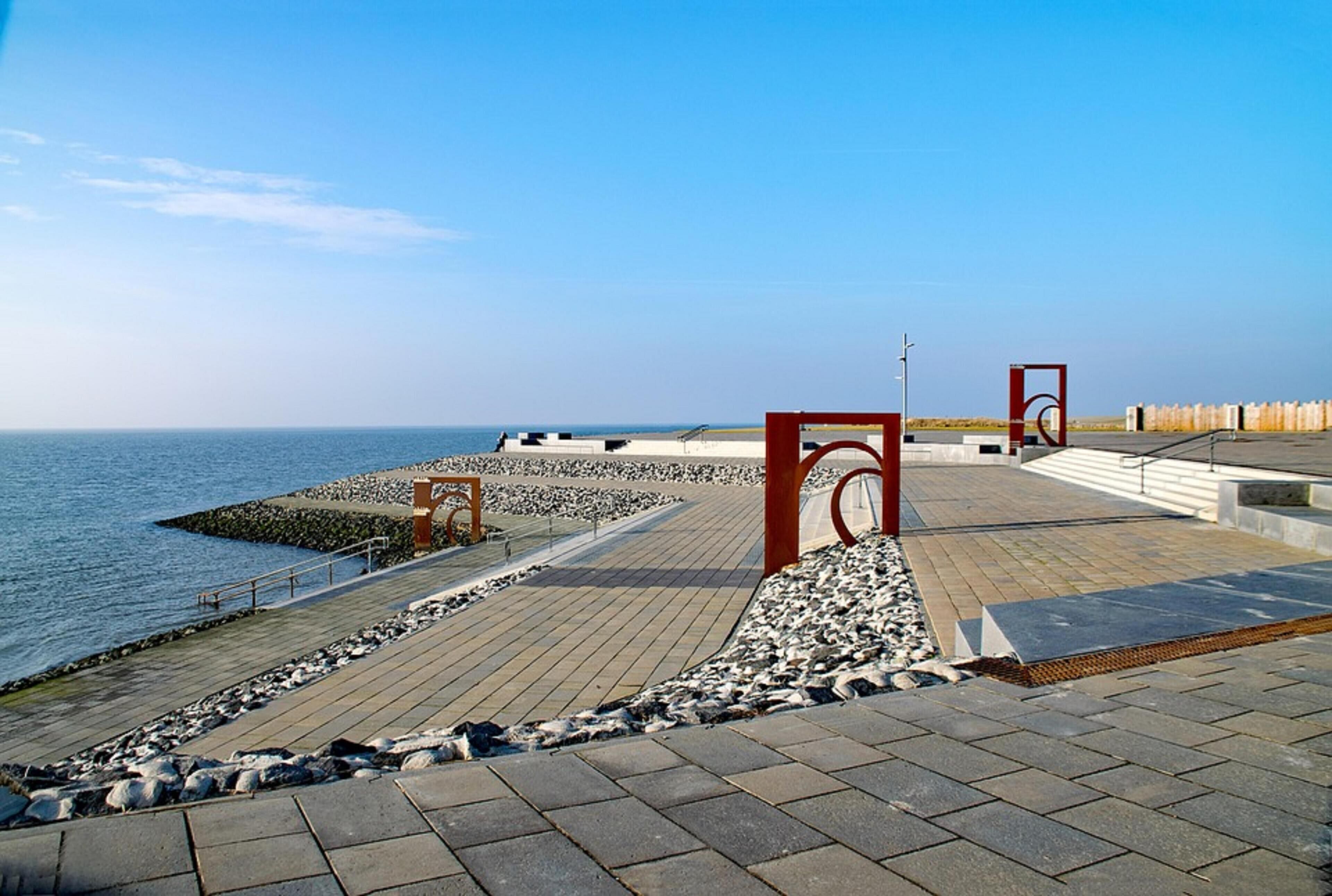 A coastal promenade with a paved walkway, a rocky shoreline, and a clear view of the sea.
