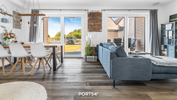 A modern living room with a sofa, dining table, and chairs. There is a large window with a view of the outdoors.
