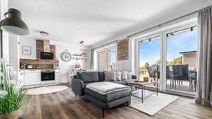 A modern living room with a grey sofa, a dining area with a table and chairs, and a kitchen in the background.