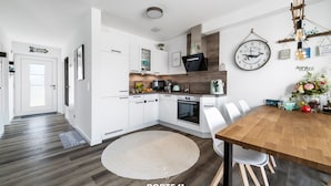 A modern kitchen with white cabinets, a wooden dining table, and a round rug.