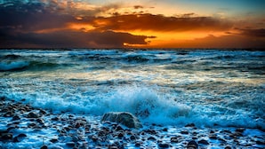 A beach with waves crashing onto rocks and a sunset in the background.