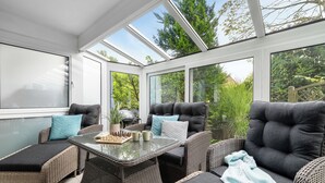 A sunroom with wicker furniture, a glass table, and a view of greenery.