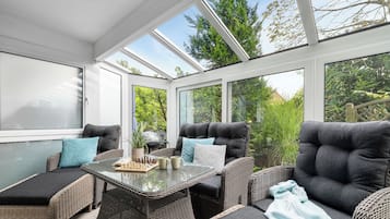 A sunroom with wicker furniture, a glass table, and a view of greenery.