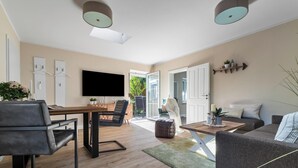 A modern living room with a dining area, a sofa, a coffee table, and a TV. - Ferienwohnung Deck 3 Büsum (Büsum)
