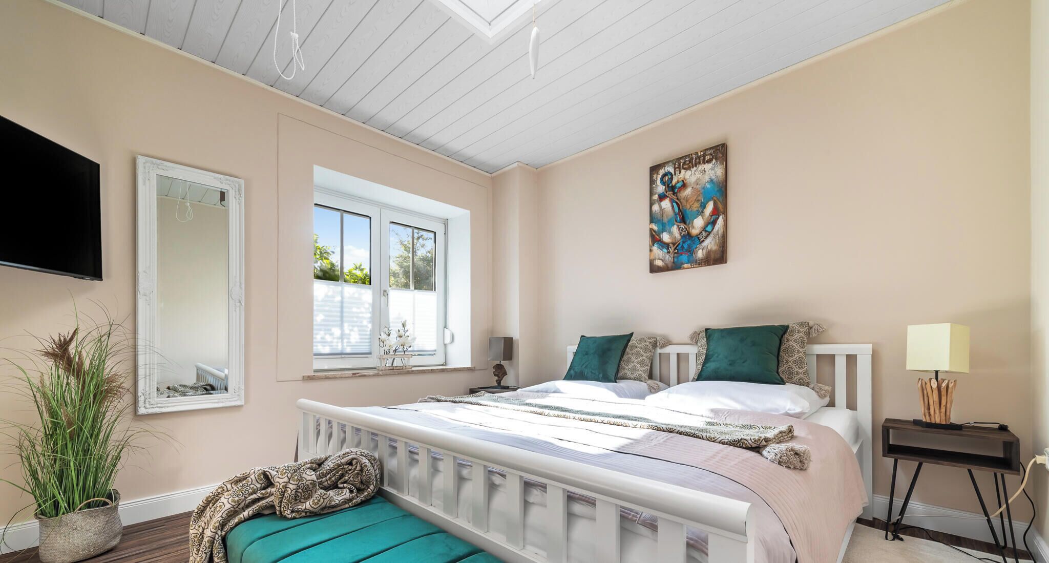 Ein Schlafzimmer mit Bett, Fenster, Gemälde, Nachttisch und Lampe.