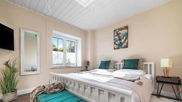 Ein Schlafzimmer mit Bett, Fenster, Gemälde, Nachttisch und Lampe.